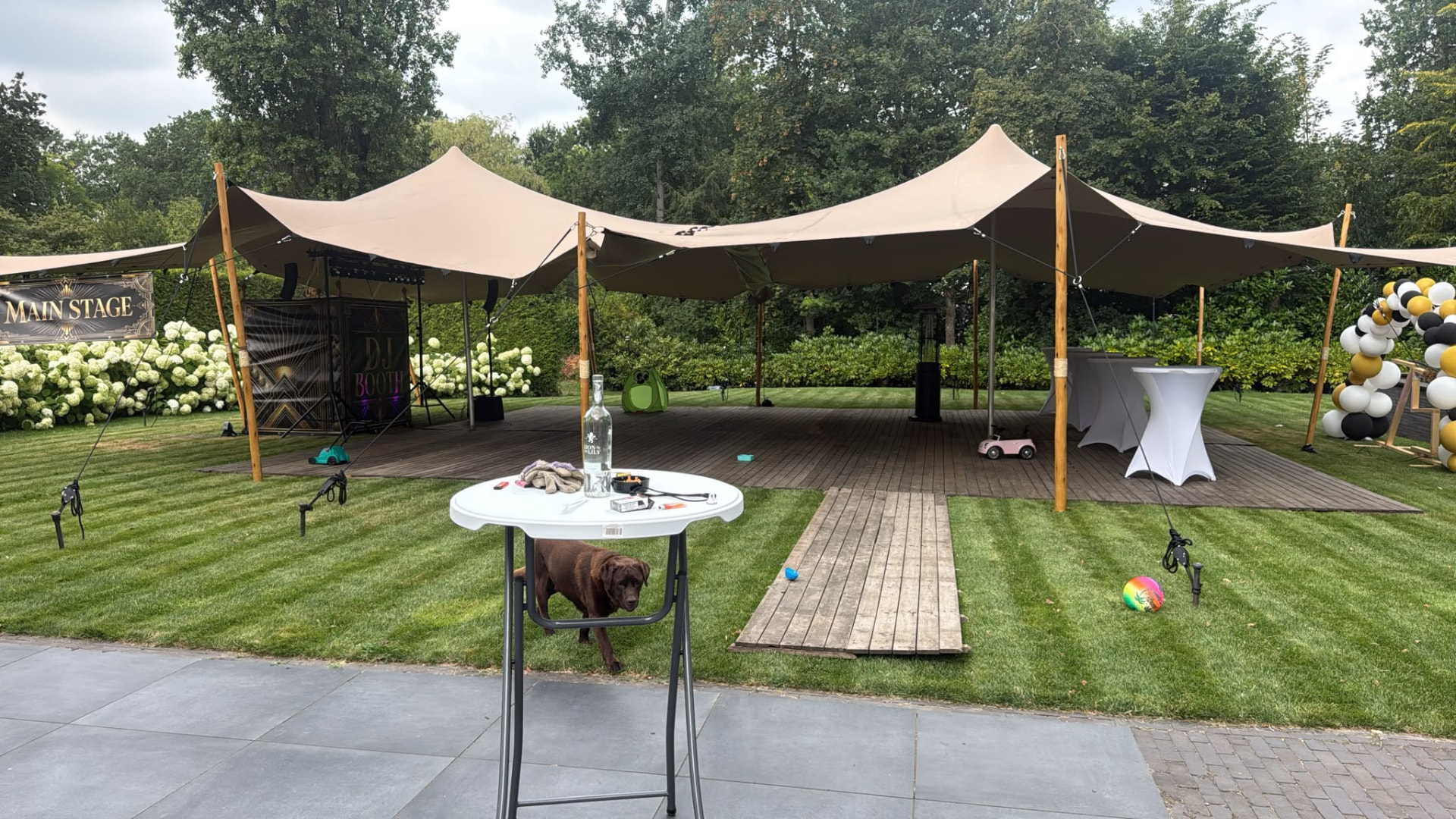 Stretchtent met statafels en dj-booth op een houten vlonder in de tuin